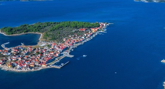 Birds-eye view of a small Croatian island partially covered by houses and trees in the blue Adriatic