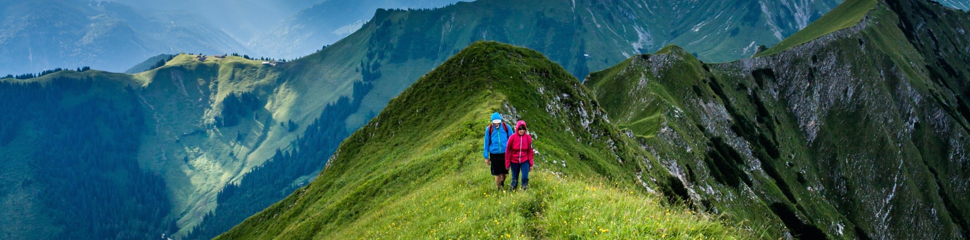 Two hikers walking on a ridge among the green mountains