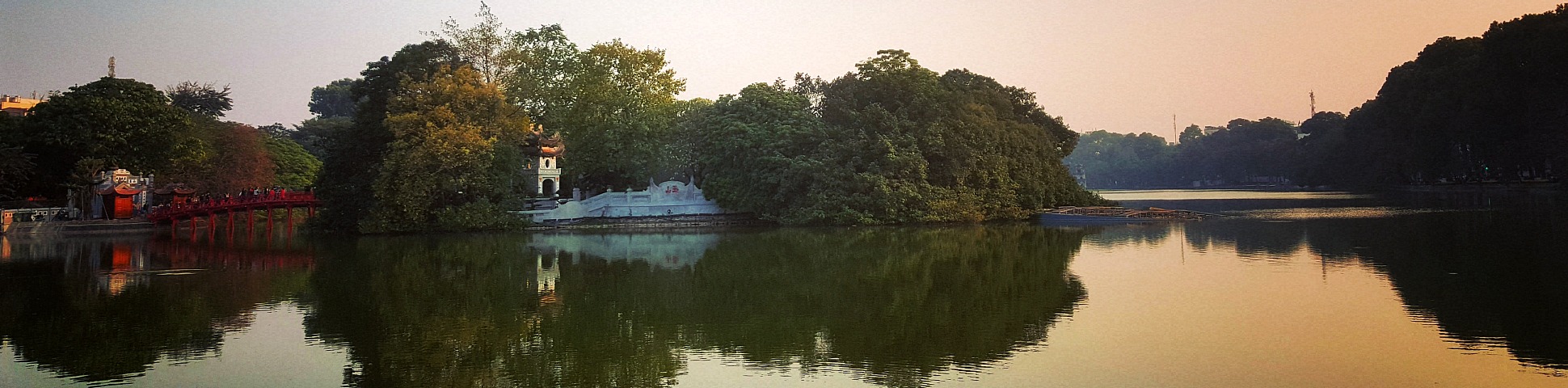 Calm river with trees, a white bulding, anda red bridge in Hanoi