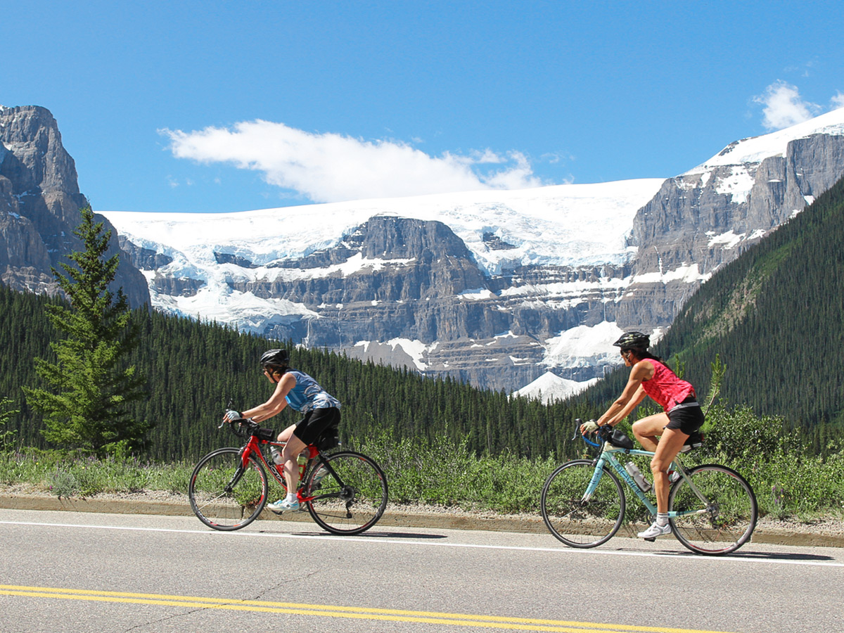 Two women biking in front of beautiful glaciers on guided cycling tour from Jasper to Banff in Canada