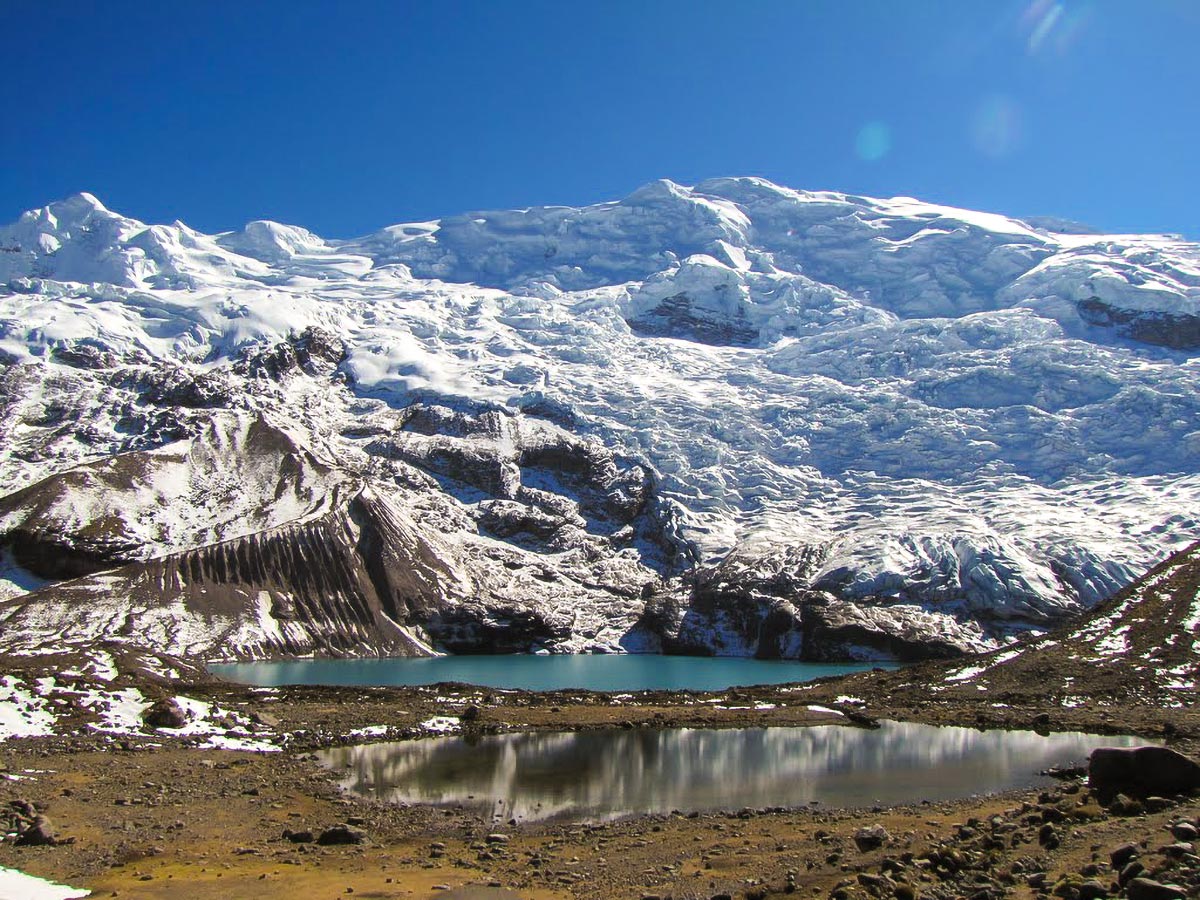 A small blue alpine lake under a snow-covered mountain in the sun