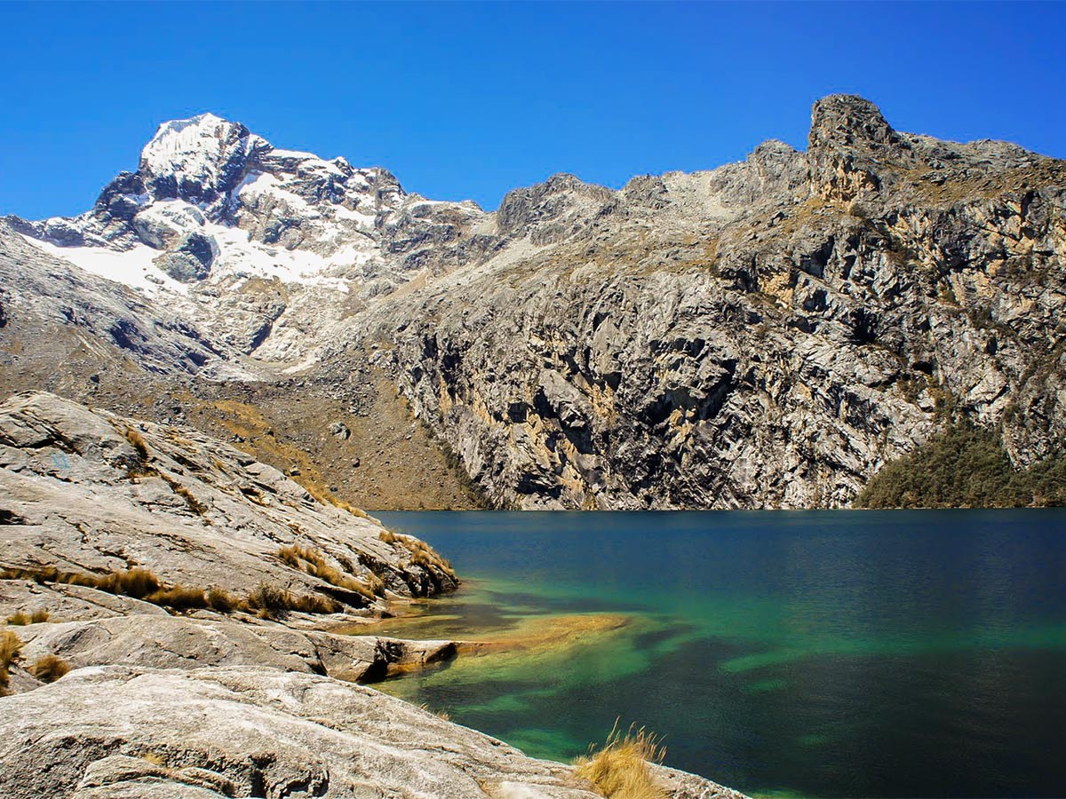 Low mountains and a blue alpine lake against blue sky