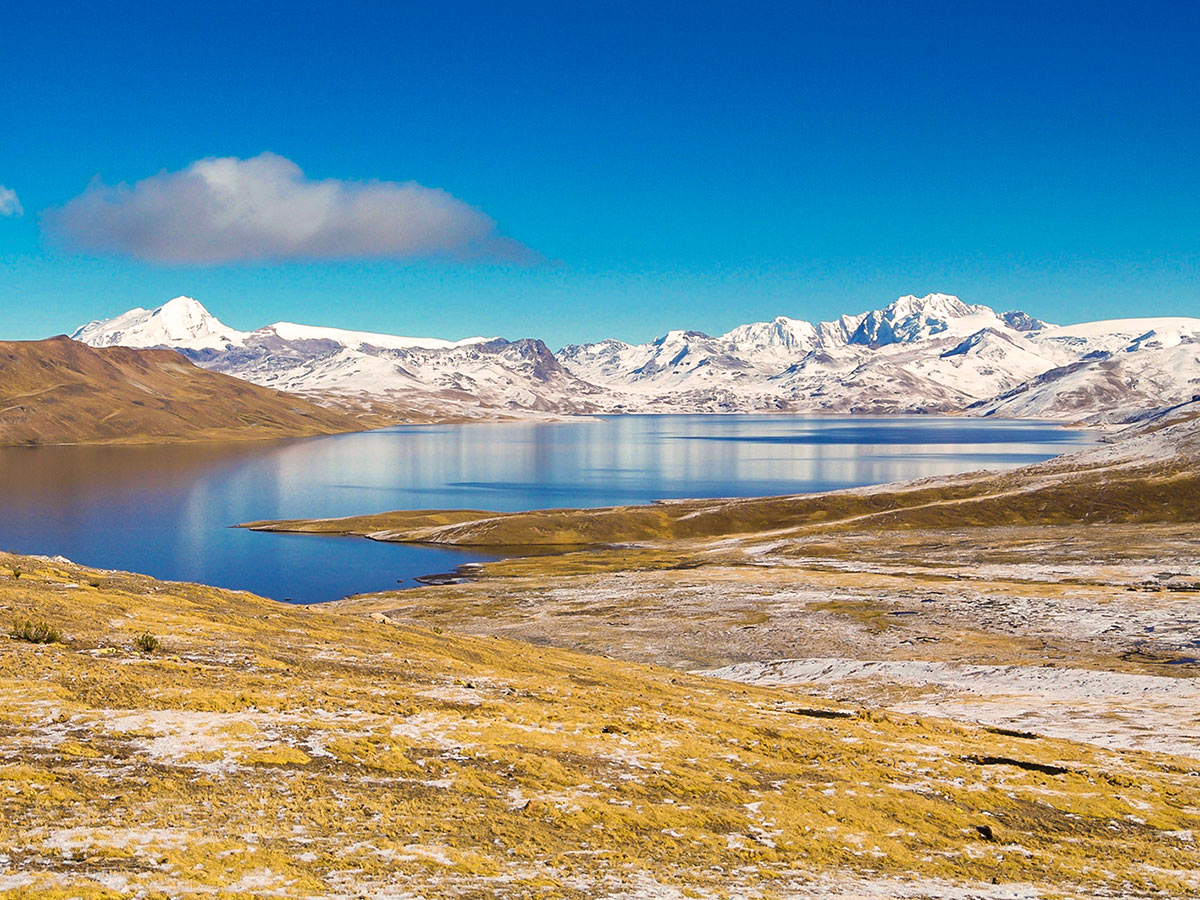 A calm blue lake surrounded by a smi-circle of low mountains covered in snow