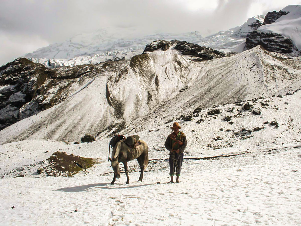 Traditionally-dressed man with a pack horse on a snow-covered mountain