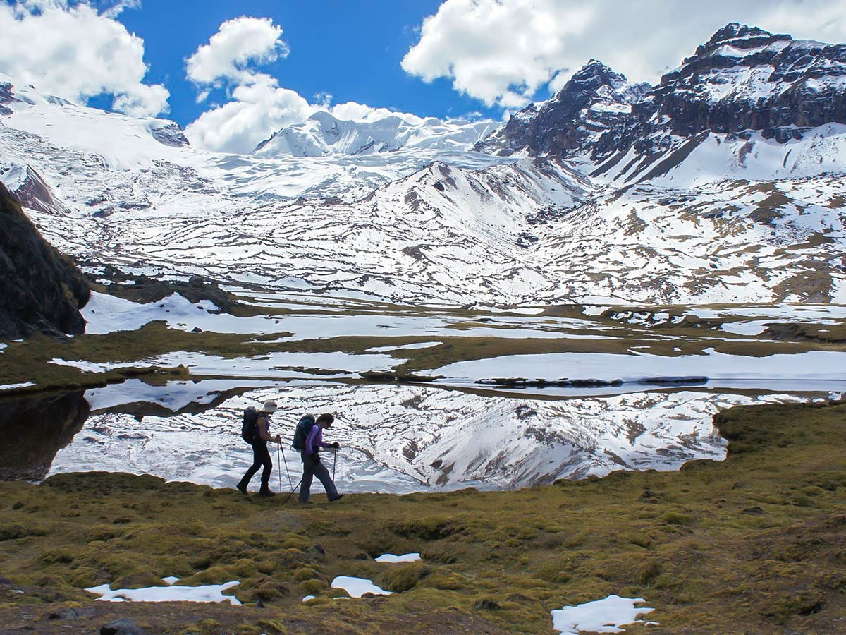 Two women trekking near several lakes with snow-covered mountains above them