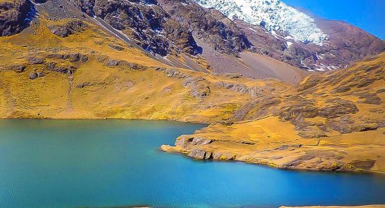 Turquoise lake surrounded by yellow hills with mountain base in the distance