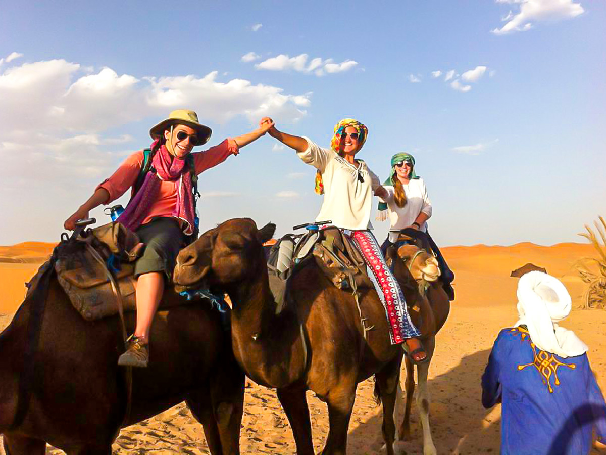 Group of happy trekkers riding camels on Merzouga Overland Tour in Morocco