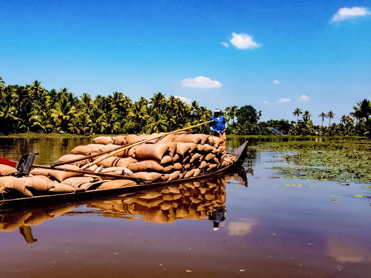 Local man transports goods on river boat seen along Kerala cycling tour India