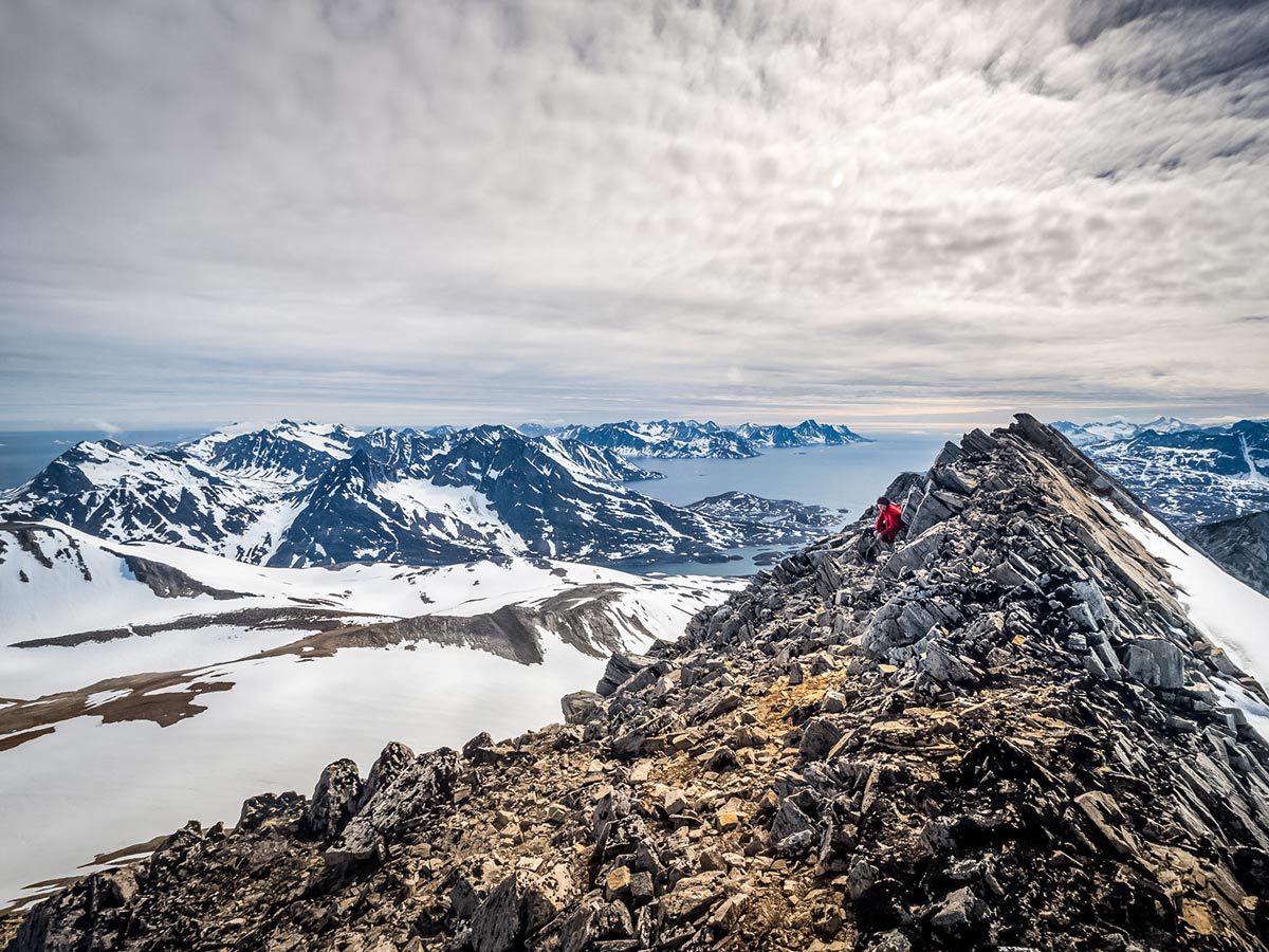 Hiker sits at rocky summit hiking in Beautiful Greenland mountians fjords