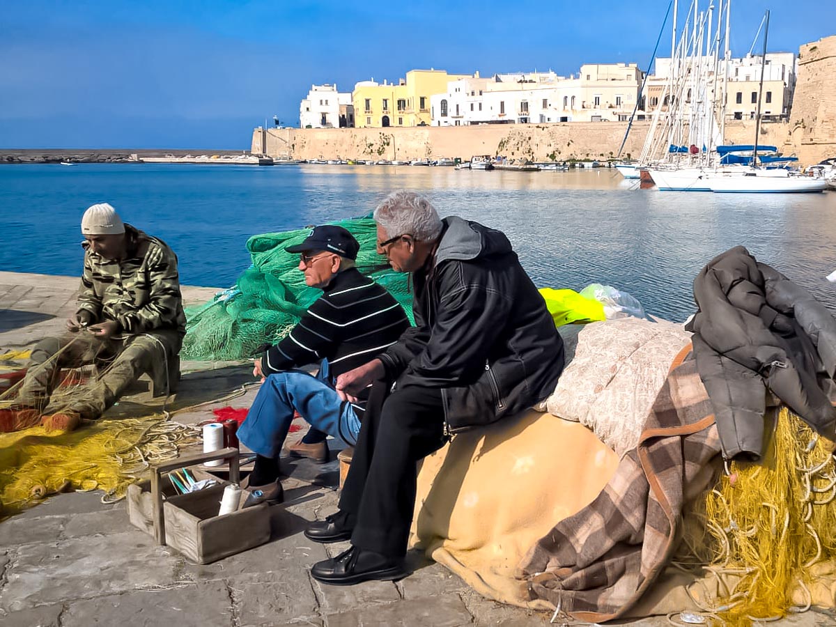 Cycling sit with fishermen on Gallipoli docks by the ocean Italy