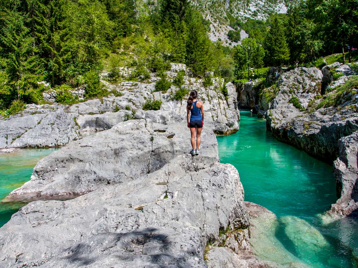 Woman exploring rocks around beautiful turquise blue river waters along mountain bikeride in Slovenia