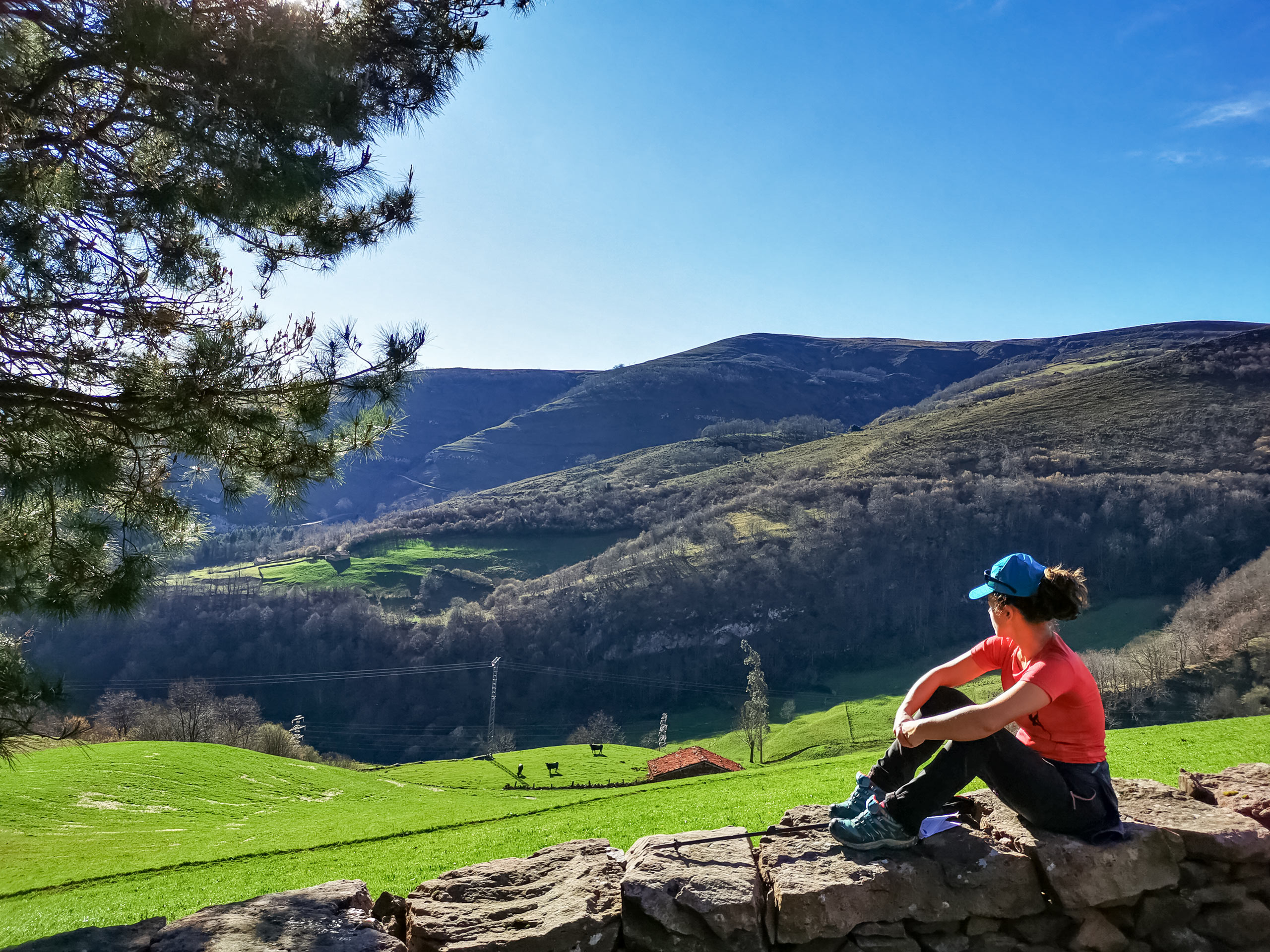 Camino Lebaniego hiker sitting on old stone rock wall looking out over farmland fields mountains Spain