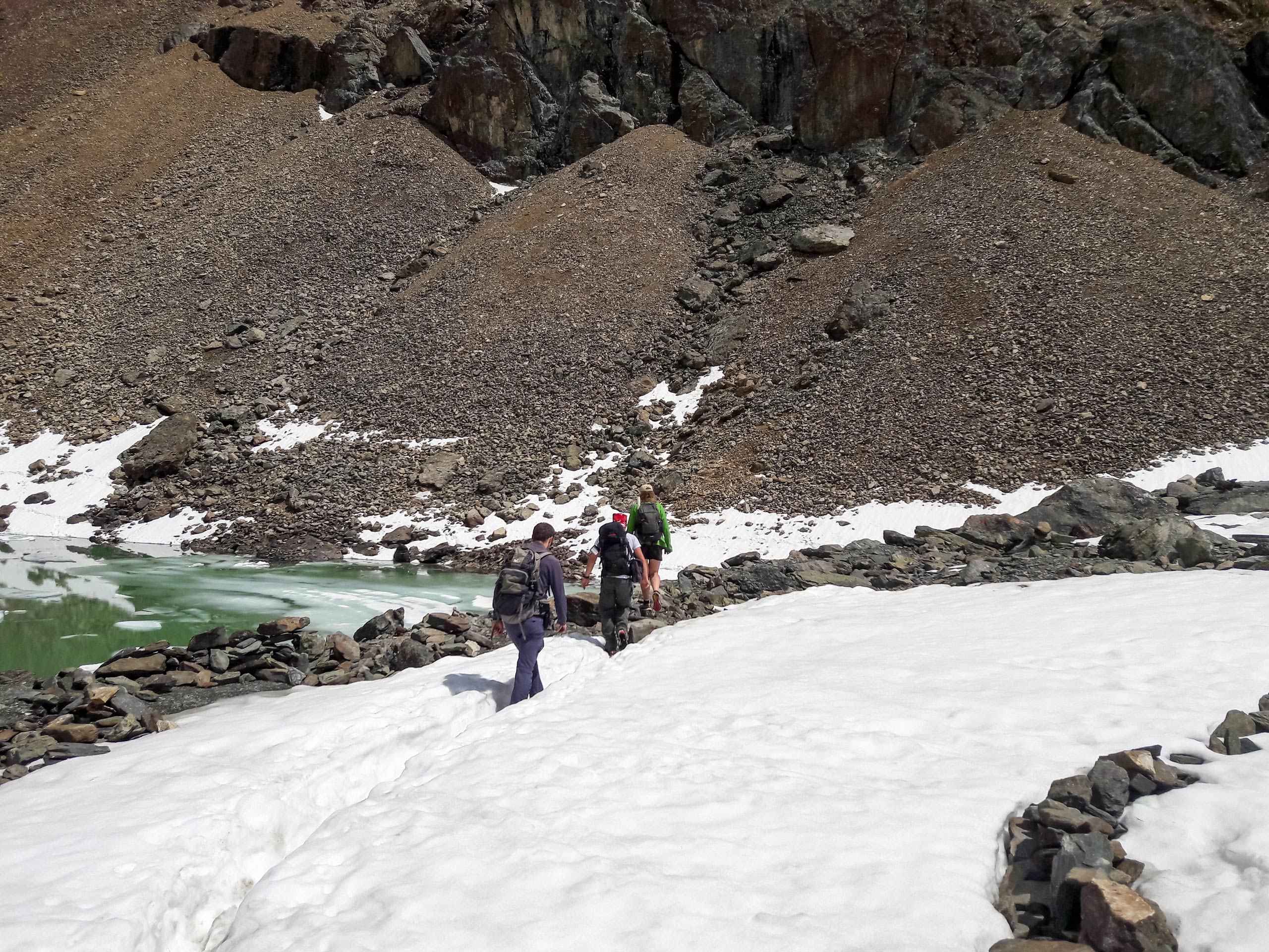 Hikers crossing glacier snow field and glacial river Altai mountains Russia