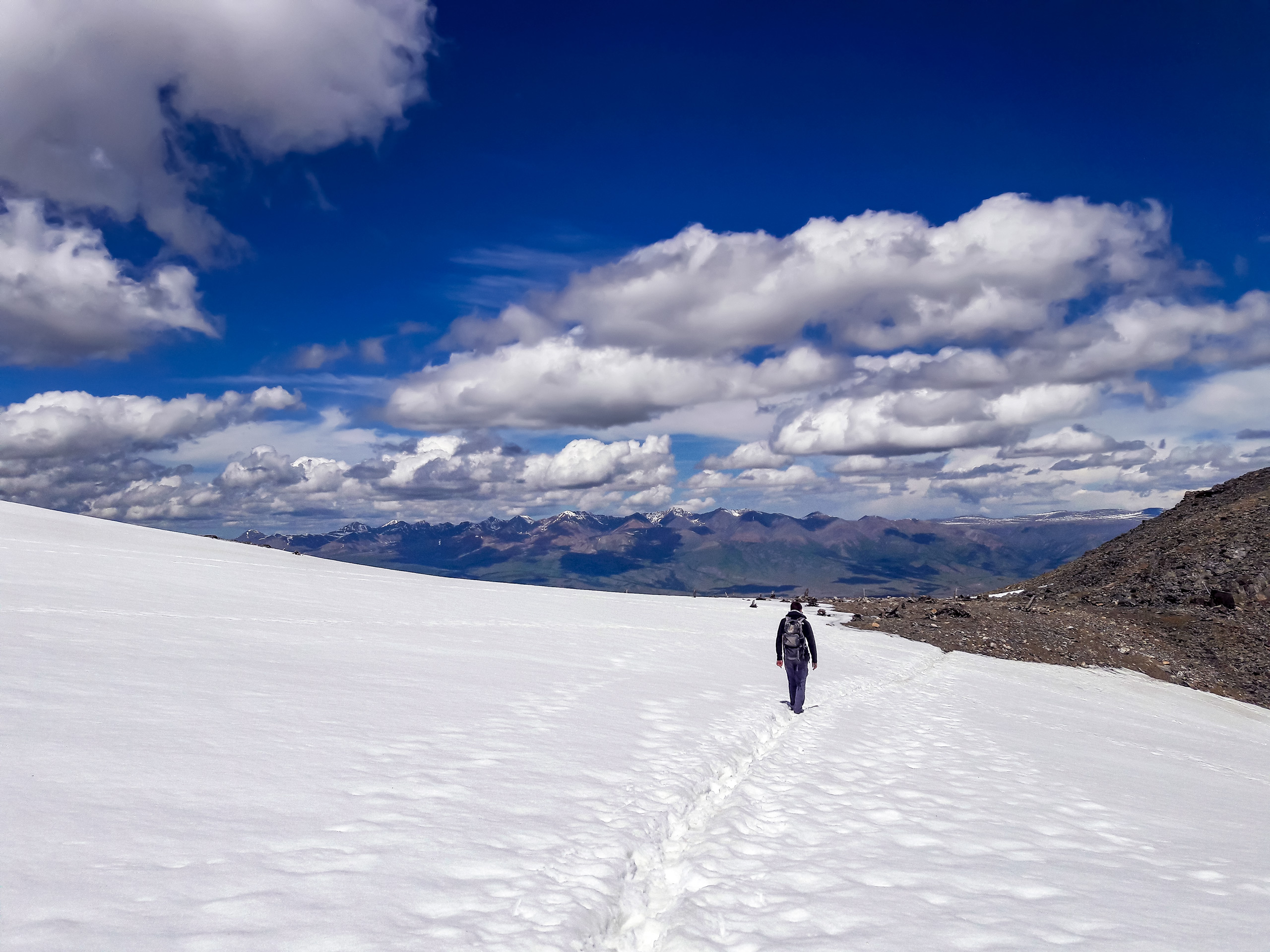 Hiker following footpath through the snow high in Altai mountains Russia