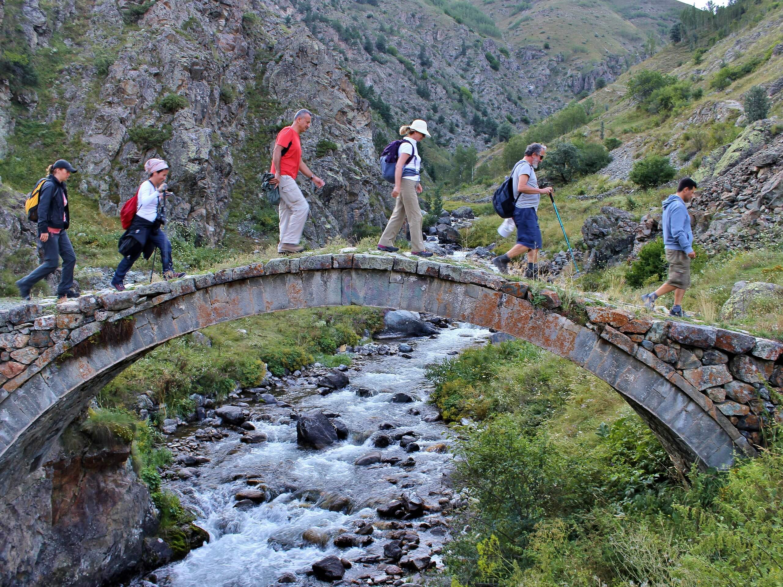 Group of trekkers crossing the creek via rock bridge in Turkey